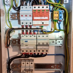 Rafał Skiba - Otwarta rozdzielnica elektryczna z uporządkowanym okablowaniem, wyłącznikami nadprądowymi, różnicowoprądowym (RCD) i ogranicznikiem przepięć (SPD) marki Hager, zamontowana na ścianie.