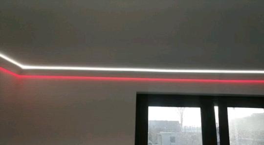 Nowoczesne oświetlenie sufitowe LED z dwoma pasami: białym i czerwonym, zamontowane wzdłuż ściany nad oknem.