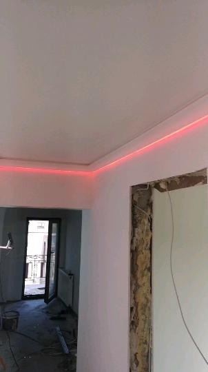 Wnętrze w trakcie remontu z podświetlonym na czerwono sufitem, widoczne ślady po usuniętych futrynach i bałagan na podłodze.