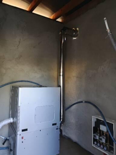 Nowoczesny piec grzewczy z odprowadzeniem spalin przez stalowy komin, zamontowany w surowym wnętrzu z widoczną instalacją hydrauliczną i skrzynką sterującą.