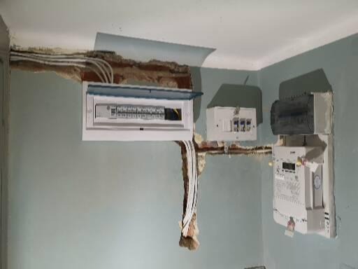 Niefachowo wykonana instalacja elektryczna: skrzynka bezpiecznikowa, licznik energii i przewody wystające ze ściany z widocznymi uszkodzeniami tynku.