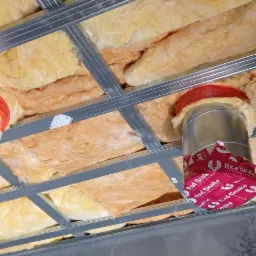 Ocieplenie poddasza wełną mineralną z widocznymi srebrnymi profilami konstrukcyjnymi i izolacją rur wentylacyjnych z czerwonymi etykietami Red Snake.