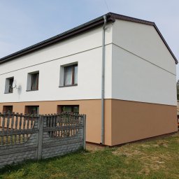 EKO-DOM Kamil Stańczyk - Dwukondygnacyjny dom po ociepleniu i pomalowaniu elewacji w kolorach biały i brązowy, z widocznym fragmentem betonowego ogrodzenia i satelitą na ścianie.