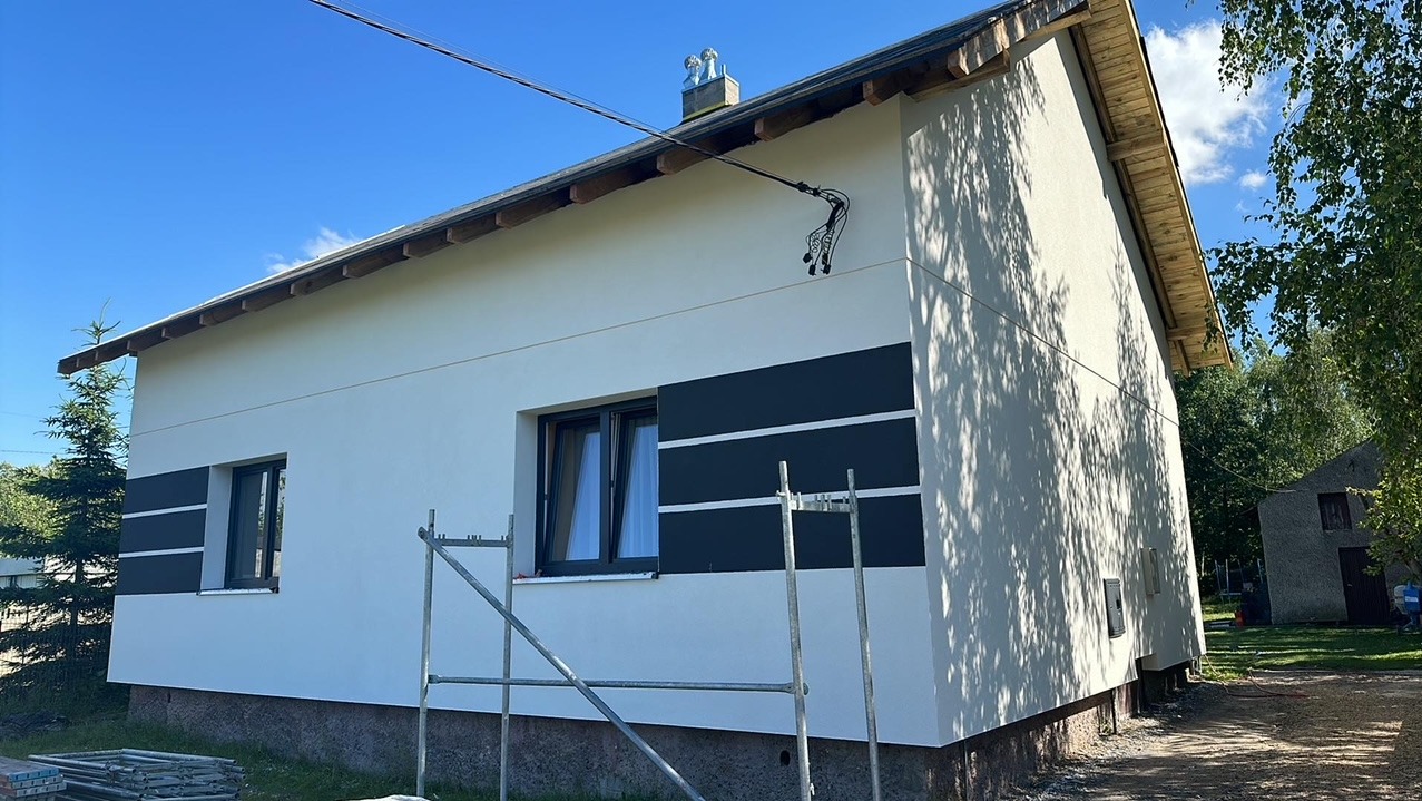 Dom po wykonaniu elewacji w kolorze białym z czarnymi pasami. Na dachu widoczna rzeźba. Ujęcie z dołu, widoczne rusztowania.