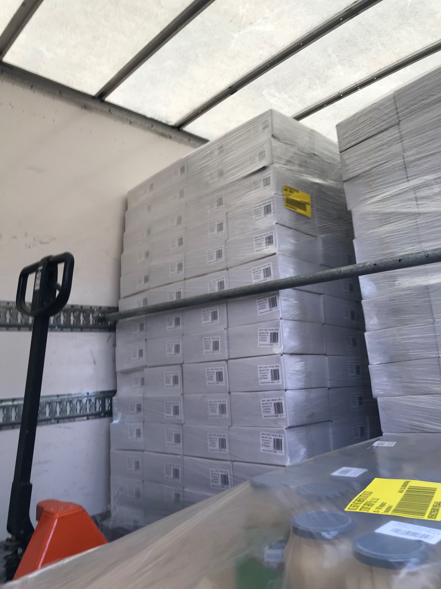 Wnętrze przestrzeni ładunkowej z paletami zapakowanych kartonów, zabezpieczonych folią stretch, widoczny wózek paletowy