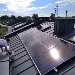 Niedźwiedź-Sanit Sp.J. - Montaż paneli słonecznych na dachu z blachy, widoczne odbicie słońca na panelach, instalator w trakcie pracy.