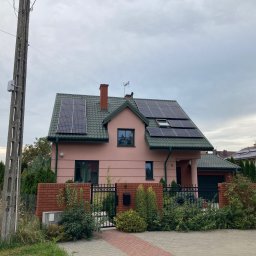 Niedźwiedź-Sanit Sp.J. - Różowy dom jednorodzinny z zielonym dachem i panelami słonecznymi, widok z ulicy w pochmurny dzień.