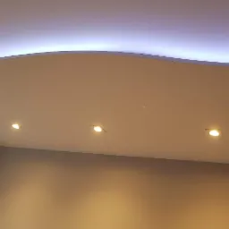 Sufit podwieszany z falistym kształtem i podświetleniem LED oraz trzema punktowymi lampami halogenowymi.