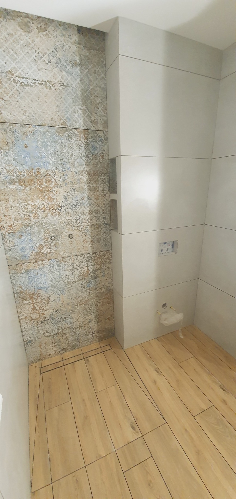 Ukończona łazienka z dekoracyjnymi płytkami ściennymi w odcieniach beżu i błękitu oraz podłogą wyłożoną panelami imitującymi drewno, widoczny odpływ liniowy.