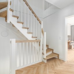 RSIFurniture - Jasne drewniane schody z białymi balustradami w nowoczesnym wnętrzu. Parkiet w jodełkę, widok na pokój z biurkiem i oknem. Minimalistyczny design, neutralna kolorystyka.