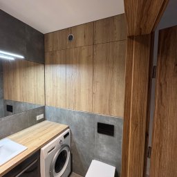 RSIFurniture - Nowoczesna łazienka z drewnianymi szafkami, blatem i drzwiami. Umywalka, pralka i toaleta wkomponowane w szaro-drewnianą aranżację. Minimalistyczny design z dbałością o detale.