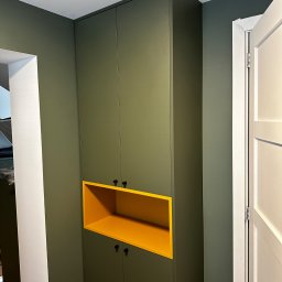 RSIFurniture - Wysoka szafa wnękowa z żółtą wnęką w Szczecinie, dopasowana kolorystycznie do ścian. Minimalistyczne czarne uchwyty, białe drzwi po prawej stronie.