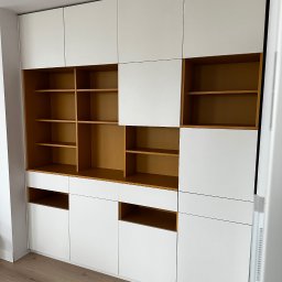 RSIFurniture - Biała zabudowa meblowa z otwartymi półkami w kolorze drewna, widok z dołu, minimalistyczny design, surowa żarówka na suficie, parkiet na podłodze.
