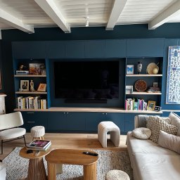 RSIFurniture - Niebieska zabudowa meblowa z półkami i szafkami, integrująca telewizor w salonie. Jasne drewno półek i podłogi kontrastuje z ciemnym kolorem mebli.