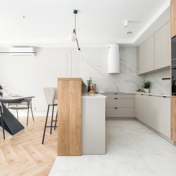 RSIFurniture - Jasna kuchnia z drewnianymi akcentami: wyspa, szafki, sprzęt AGD. Marmurowa ściana i podłoga. Stół z kwiatami w tle. Nowoczesny design, minimalistyczne oświetlenie.