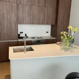 Nowoczesna kuchnia z zabudową z ciemnego drewna, białą wyspą z wbudowanym zlewem i kwiatami w wazonach na blacie