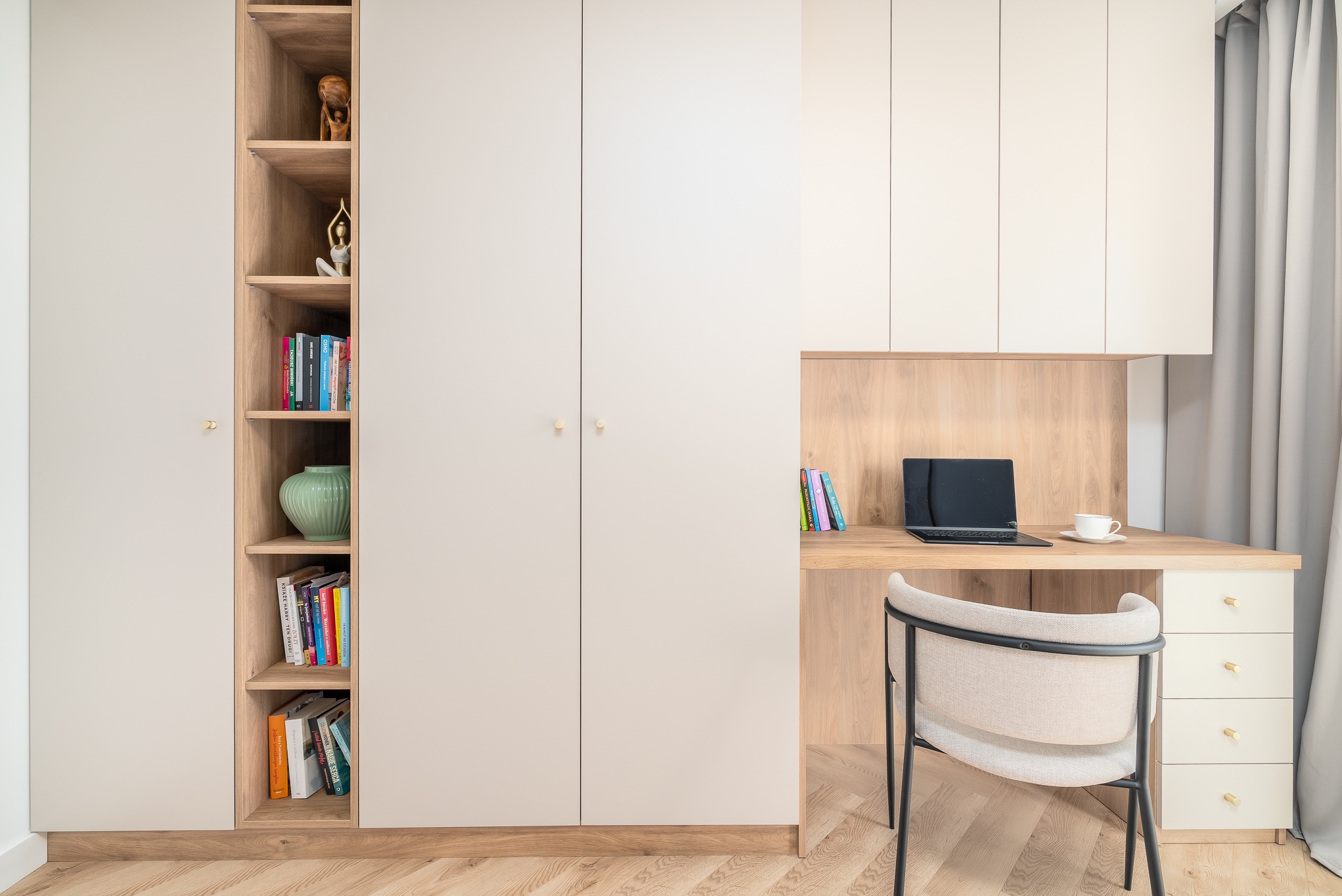 Biała szafa wnękowa z biurkiem i półkami w odcieniach drewna, z dekoracjami i książkami. Realizacja w Szczecinie, minimalistyczny design, złote uchwyty.