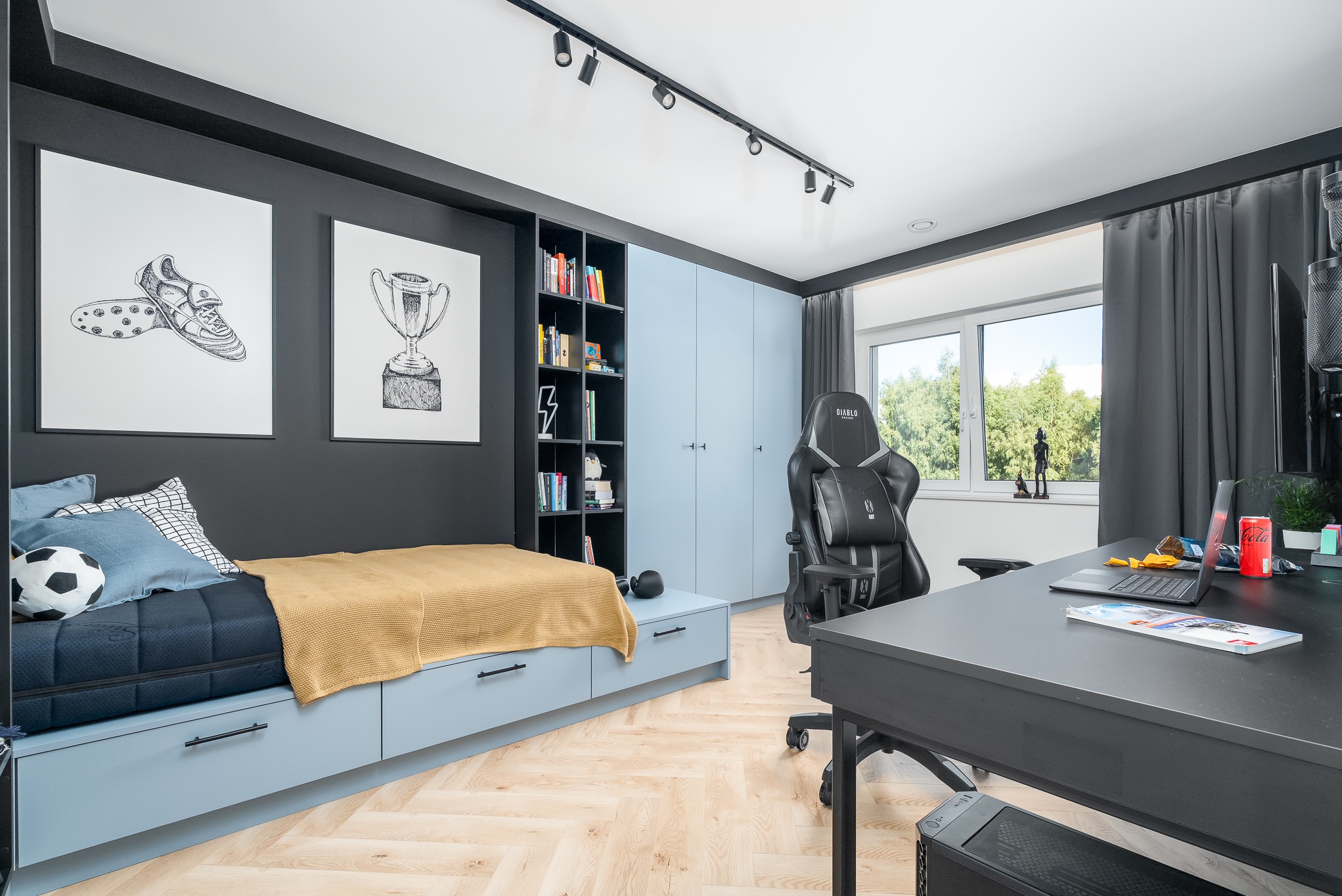 Pokój młodzieżowy w chłodnych barwach: łóżko z szufladami, szafa, biurko z komputerem, fotel gamingowy, plakaty o tematyce sportowej, parkiet w jodełkę.
