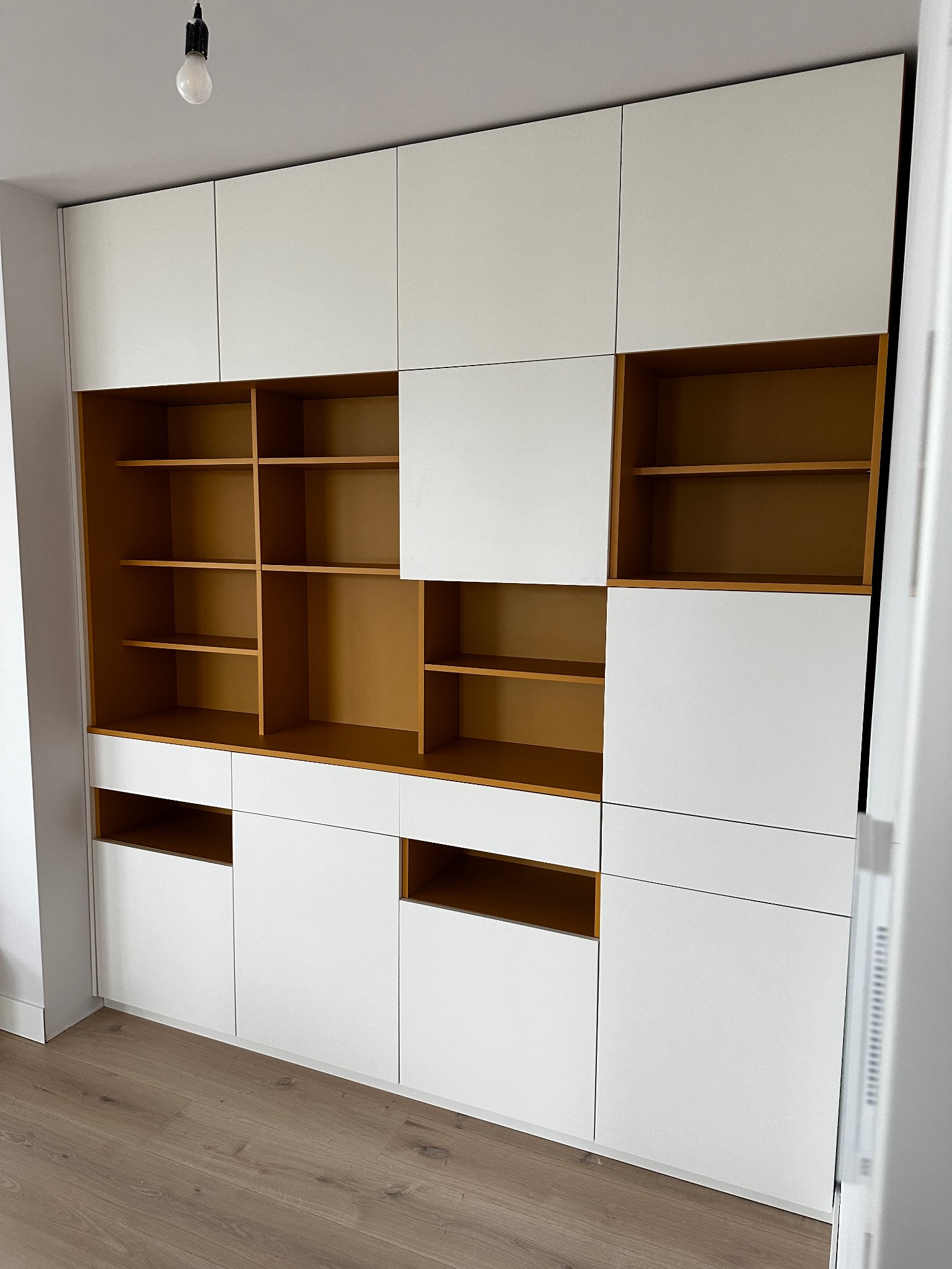 Biała zabudowa meblowa z otwartymi półkami w kolorze drewna, widok z dołu, minimalistyczny design, surowa żarówka na suficie, parkiet na podłodze.