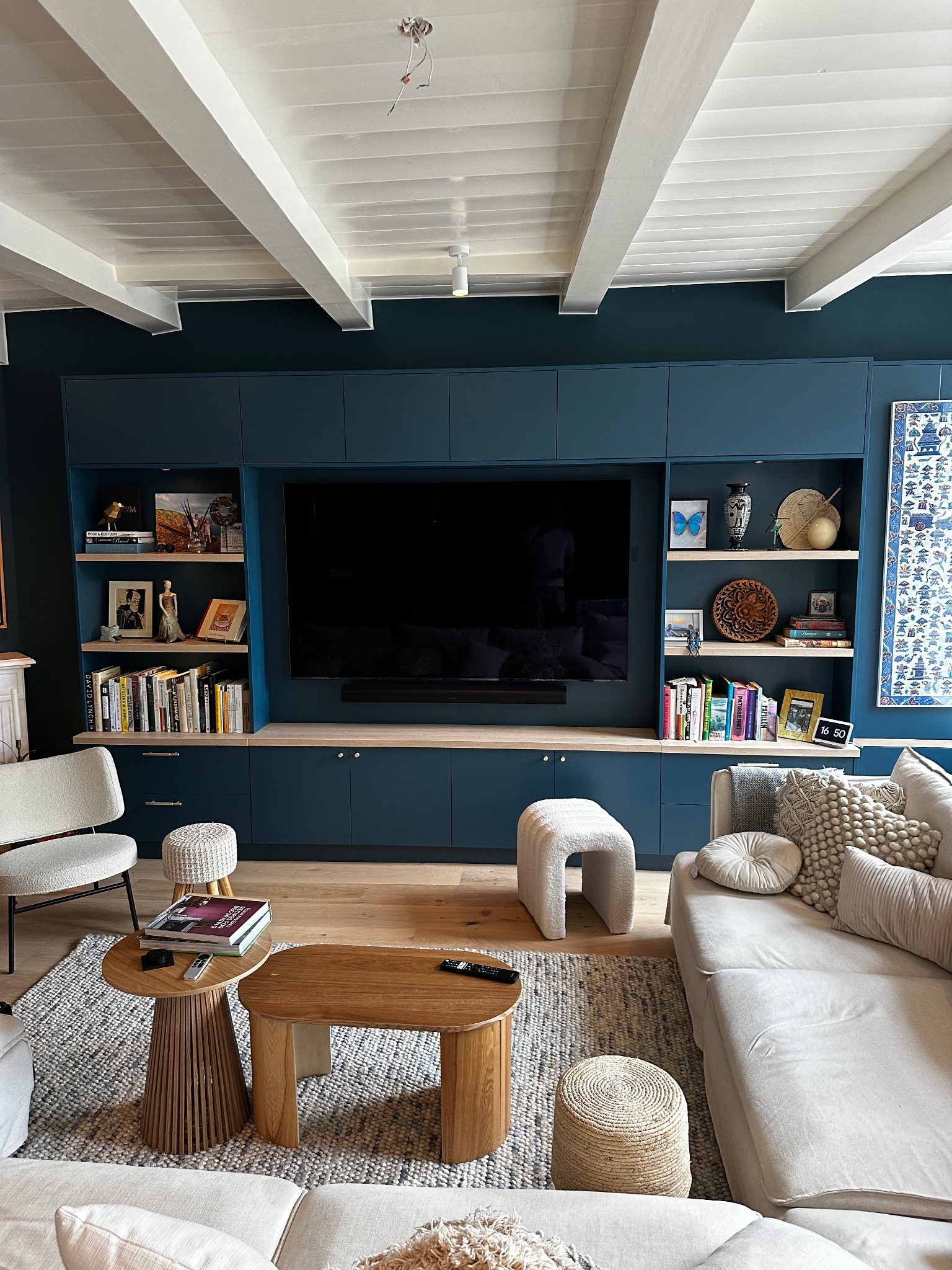 Niebieska zabudowa meblowa z półkami i szafkami, integrująca telewizor w salonie. Jasne drewno półek i podłogi kontrastuje z ciemnym kolorem mebli.