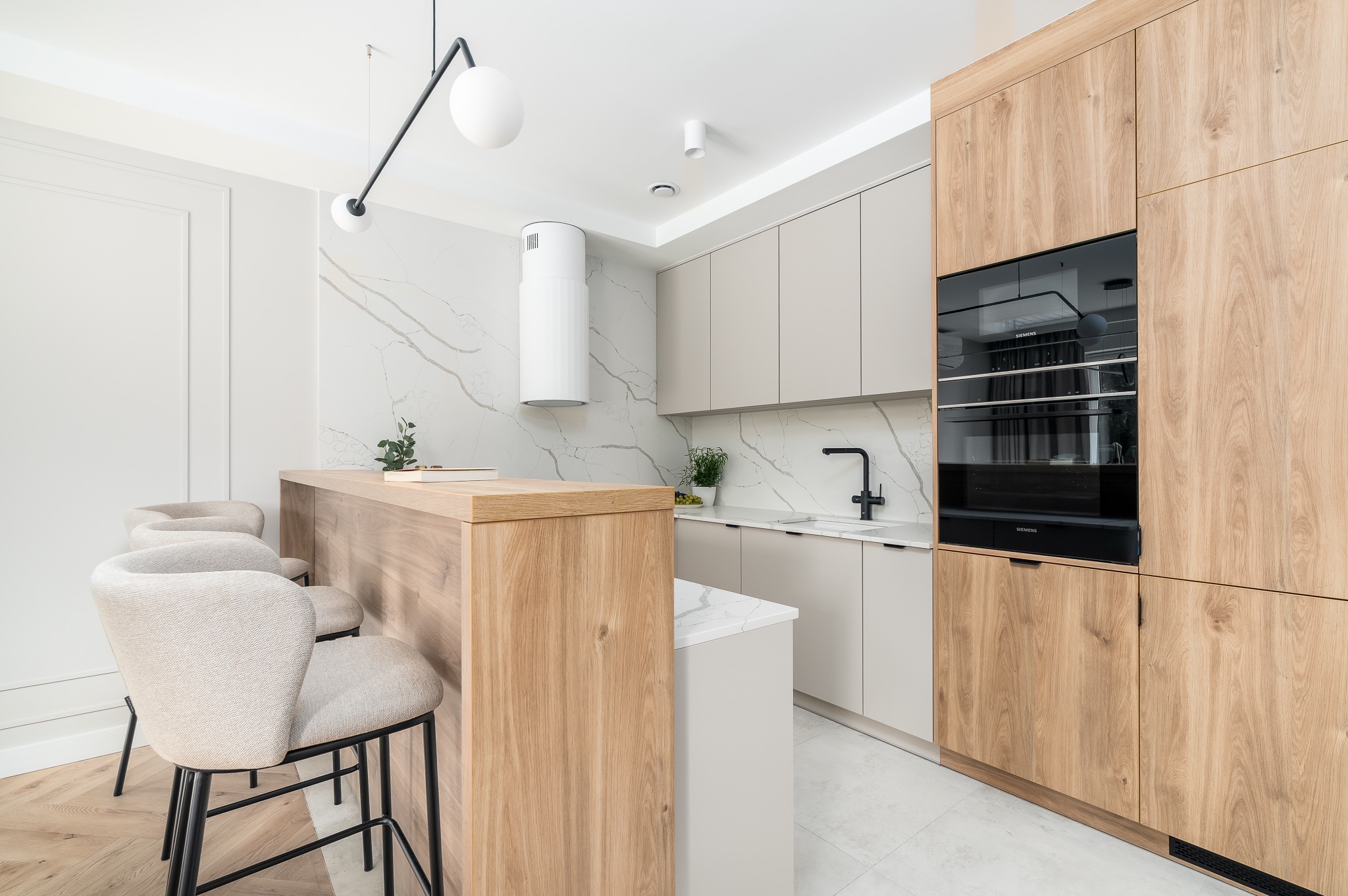 Nowoczesna kuchnia z drewnianą zabudową, wyspą i marmurowym blatem. Krzesła barowe z tapicerką. Minimalistyczny design, jasne kolory i eleganckie wykończenie.