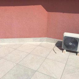 U.N.J.F. - u Nas Jest Fajnie - Zewnętrzna jednostka klimatyzacji marki Vivax zamontowana na jasnym, wykafelkowanym tarasie z różową ścianą w tle.