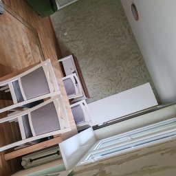 PikulBud - Ustawiony stół z krzesłami w jasnym wnętrzu z dekoracyjną ścianą. Widok na okno i grzejnik. Perspektywa z dołu, obrót o 90 stopni.