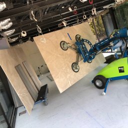 Raf-Kop - Montaż marmurowych płyt ściennych za pomocą specjalistycznego podnośnika Winlet 600 na budowie, widoczne przewody pod sufitem i duże okna.