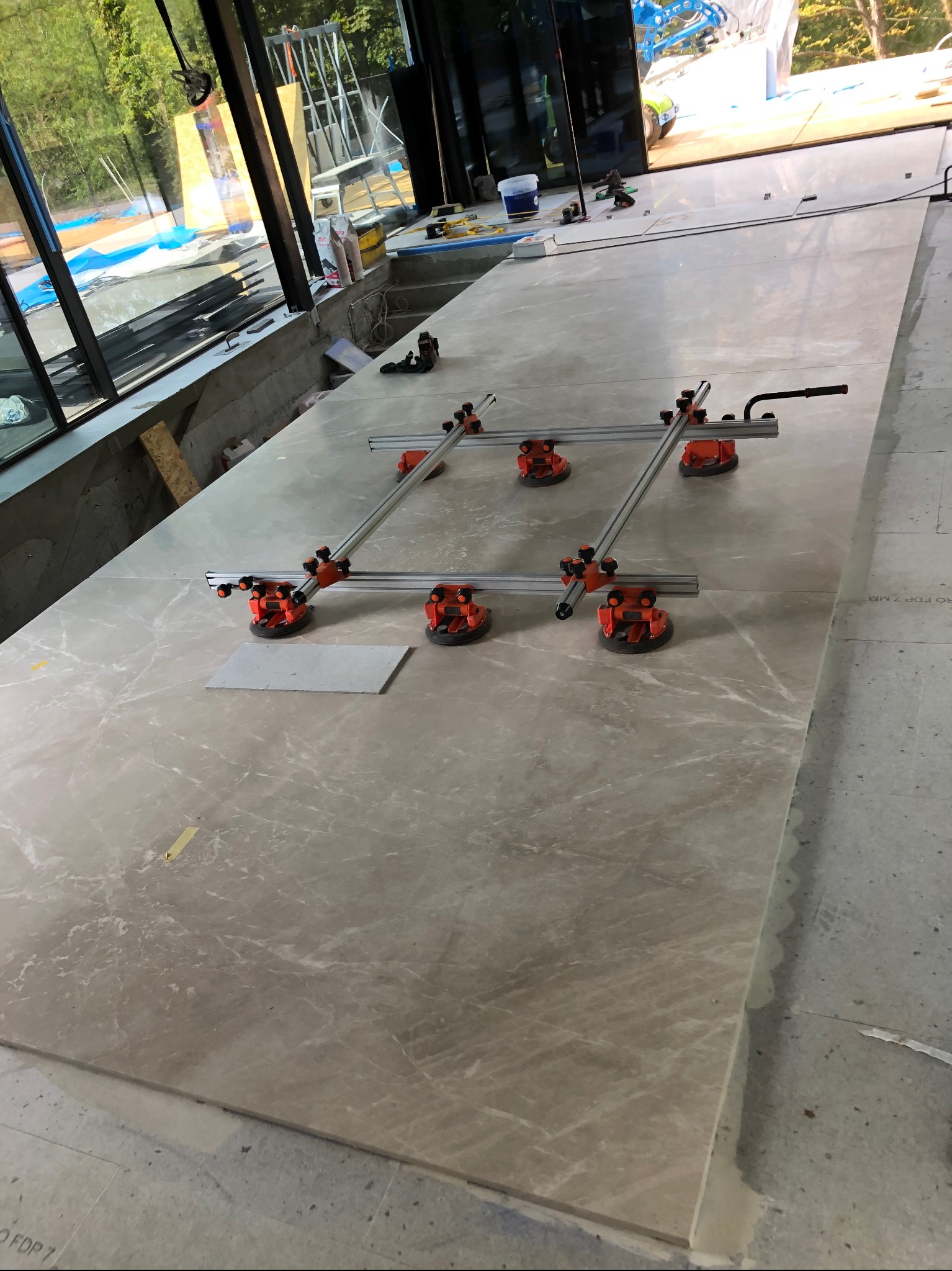 Układanie wielkoformatowych płyt z imitacją marmuru przy użyciu przyssawek i prowadnic, widoczny fragment podłogi w trakcie prac wykończeniowych.