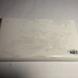 AN-MAR Parapety - Próbka białego parapetu z konglomeratu z widocznymi przetarciami i naklejką 'NB1' w prawym dolnym rogu.