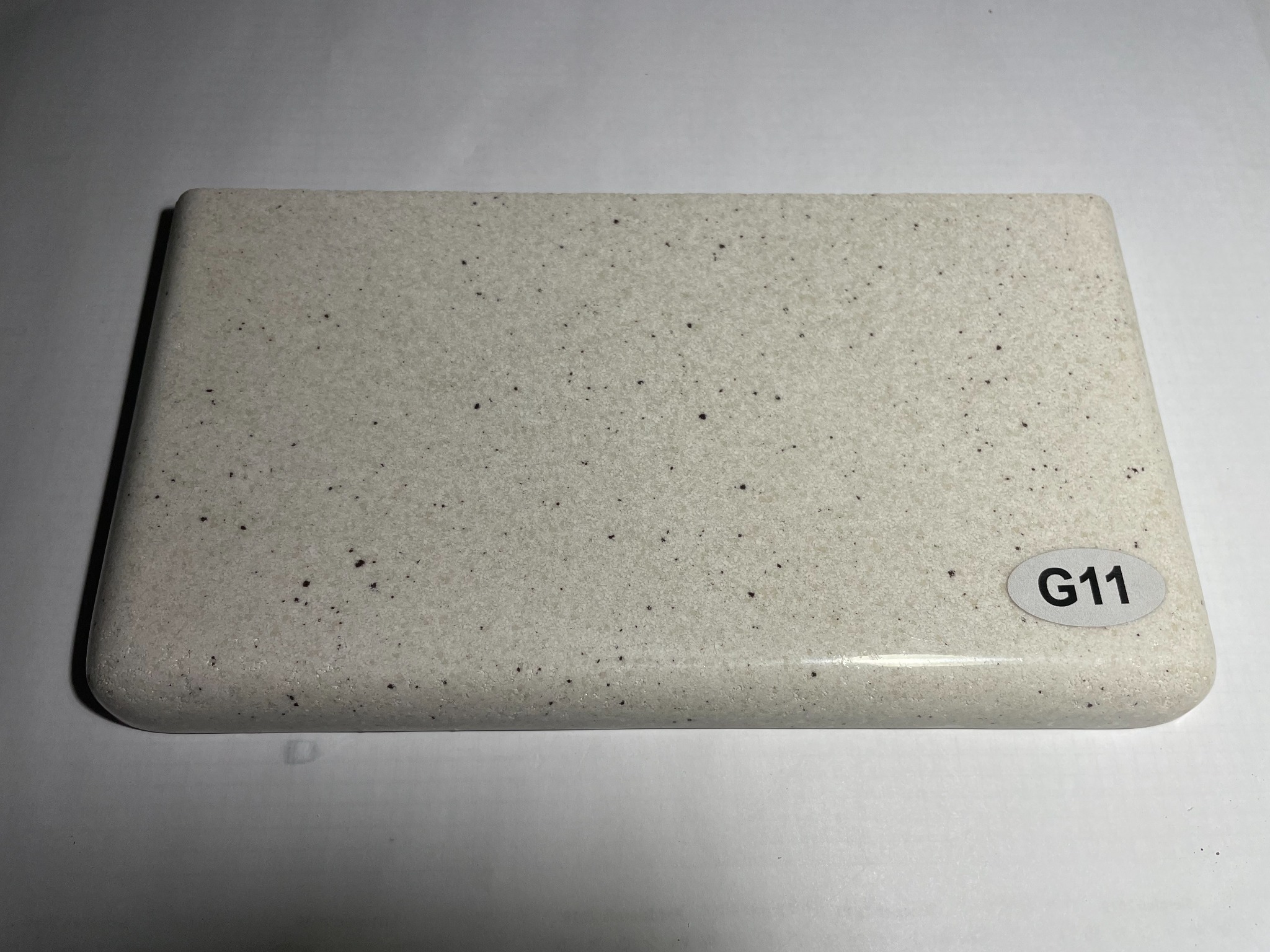 Próbka blatu o nieregularnej, nakrapianej fakturze w odcieniach bieli i szarości, z zaokrąglonymi krawędziami i oznaczeniem 'G11' na naklejce.