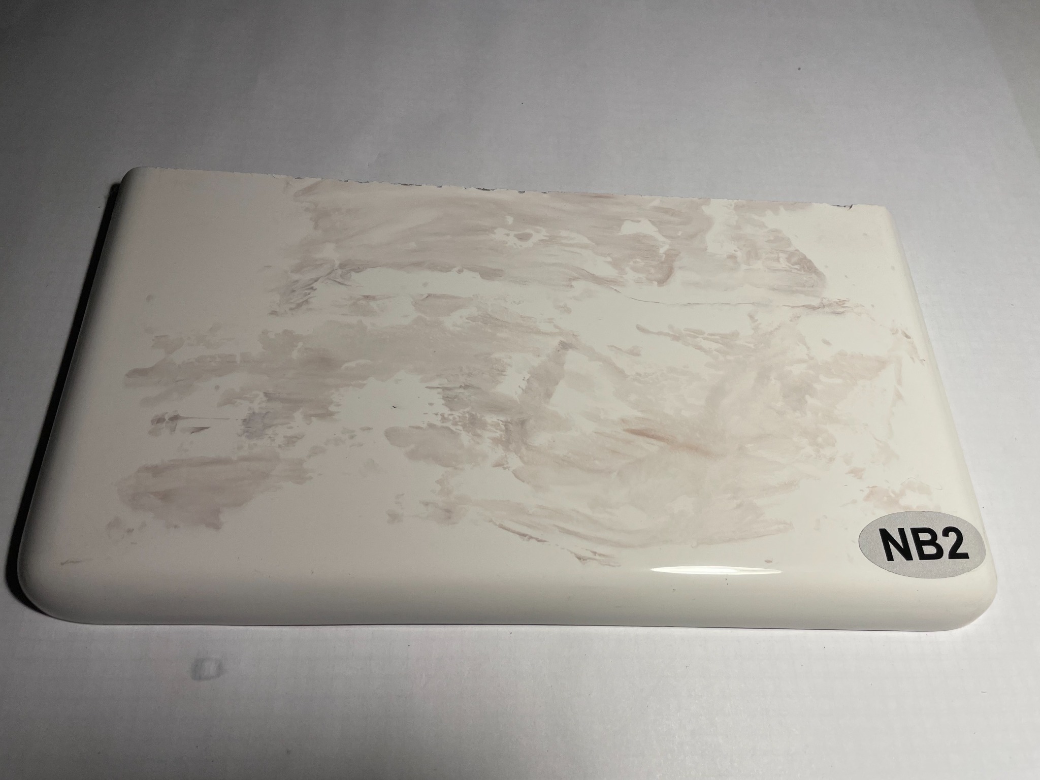 Próbka białego materiału z nieregularnymi, beżowymi wzorami przypominającymi marmur, oznaczona naklejką 'NB2'.