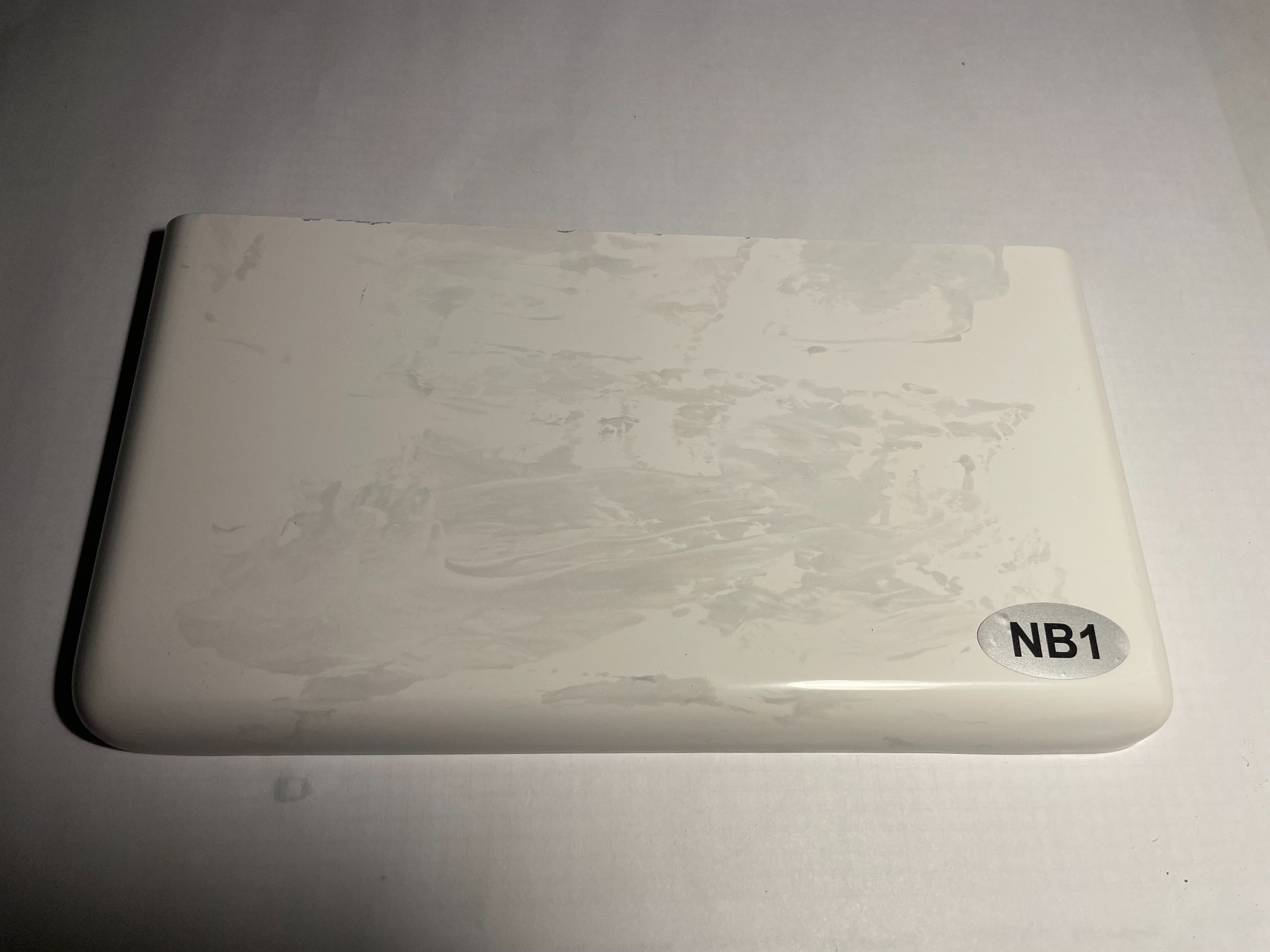 Próbka białego parapetu z konglomeratu z widocznymi przetarciami i naklejką 'NB1' w prawym dolnym rogu.