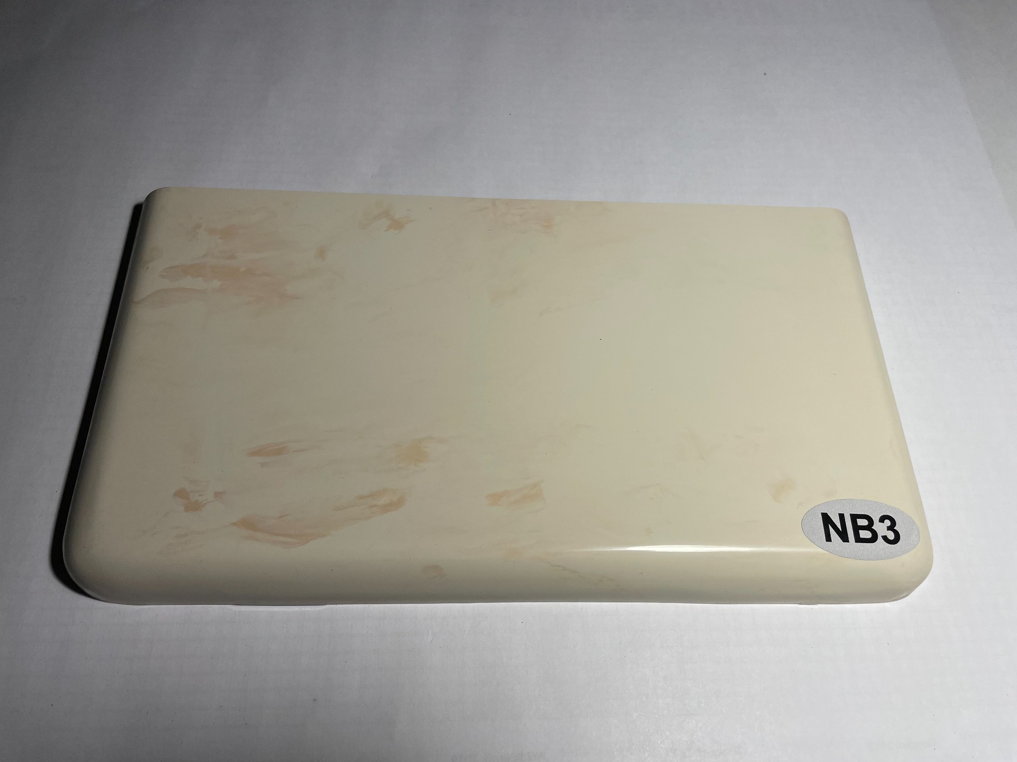 Próbka beżowego parapetu z delikatnym wzorem i naklejką 'NB3' w prawym dolnym rogu, leżąca na białym tle.