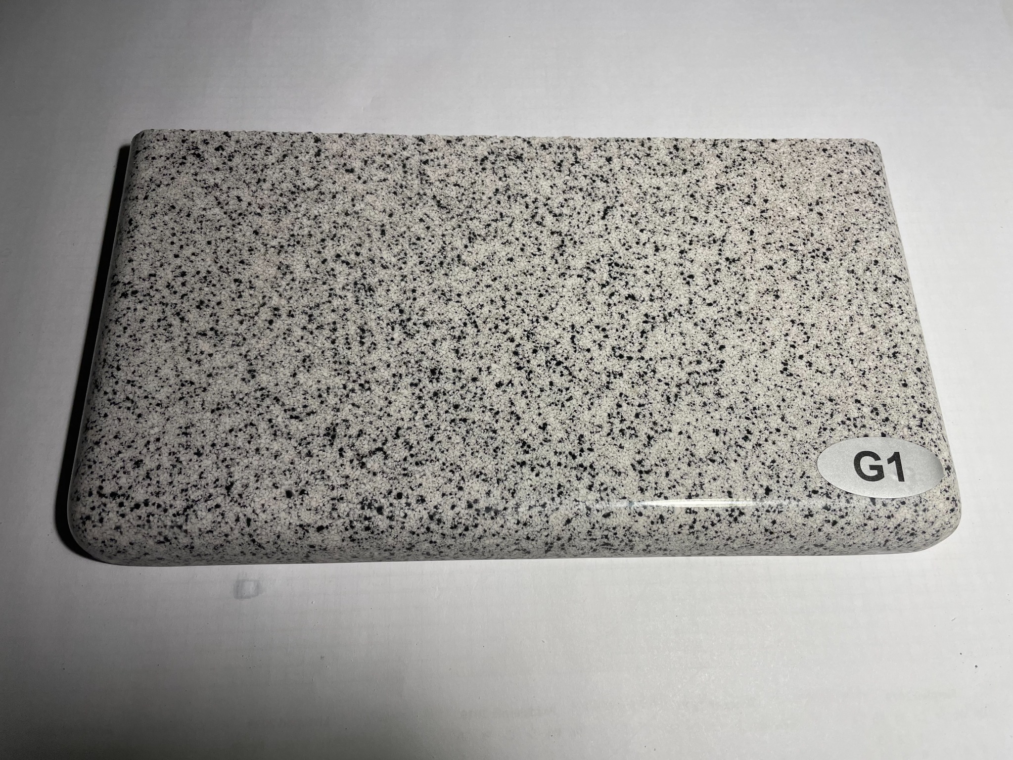 Próbka szarego parapetu z drobnymi czarnymi plamkami, oznaczona etykietą 'G1' na zaokrąglonym rogu.