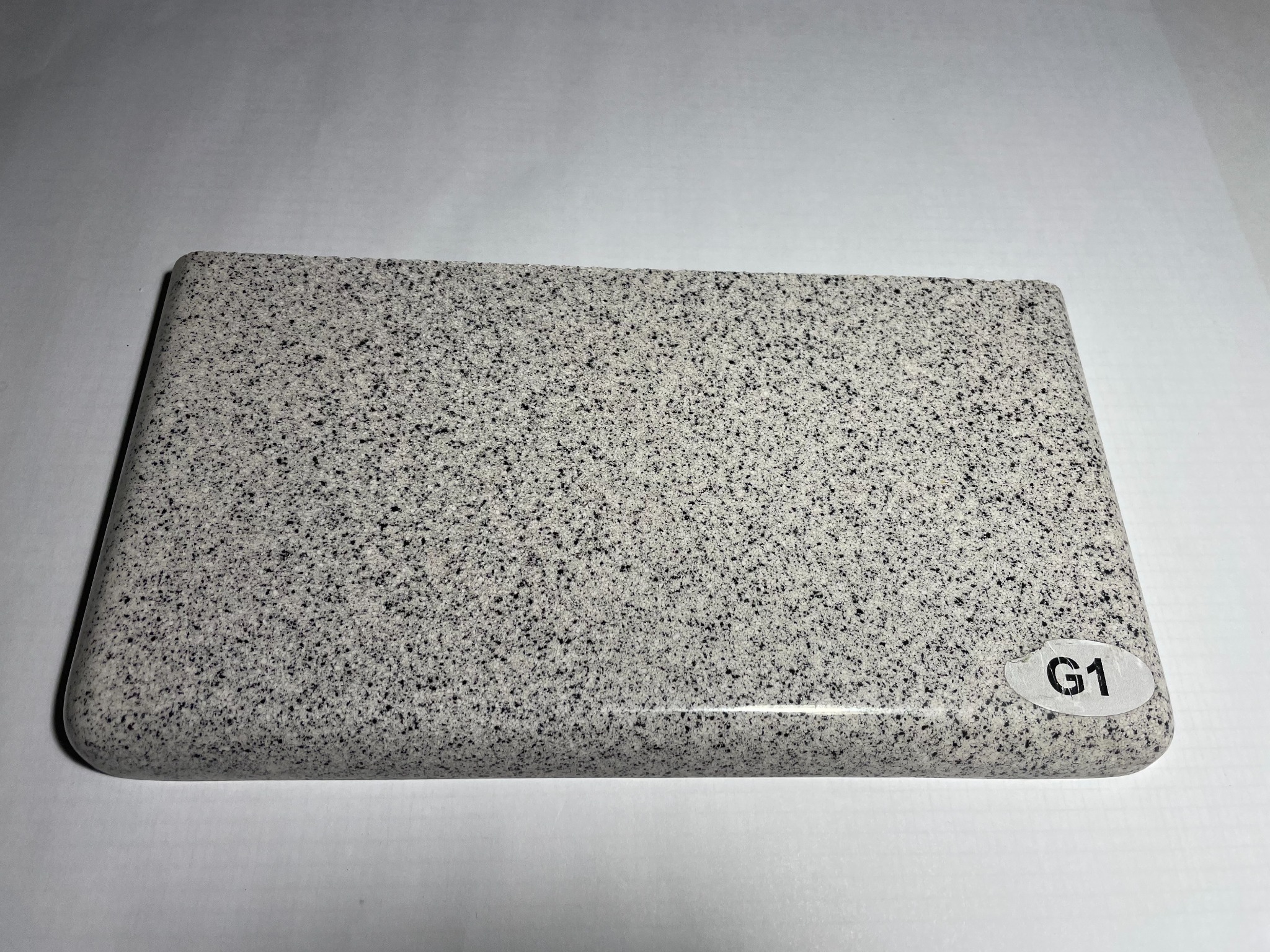 Próbka szarego blatu z drobnym czarnym wzorem, o zaokrąglonych krawędziach, leżąca na białym tle, z naklejką 'G1' w prawym dolnym rogu.