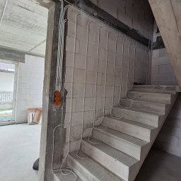 Octo-elektro - Surowe wnętrze w trakcie budowy: betonowe schody i ściany z betonu komórkowego z poprowadzonymi przewodami elektrycznymi w białych peszlach, widoczne puszki instalacyjne.