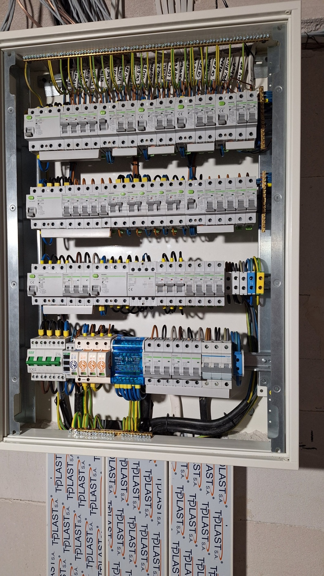 Rozdzielnica elektryczna z zainstalowanymi bezpiecznikami, przewodami oznaczonymi etykietami i elementami montażowymi, widoczna w skrzynce z tworzywa sztucznego.