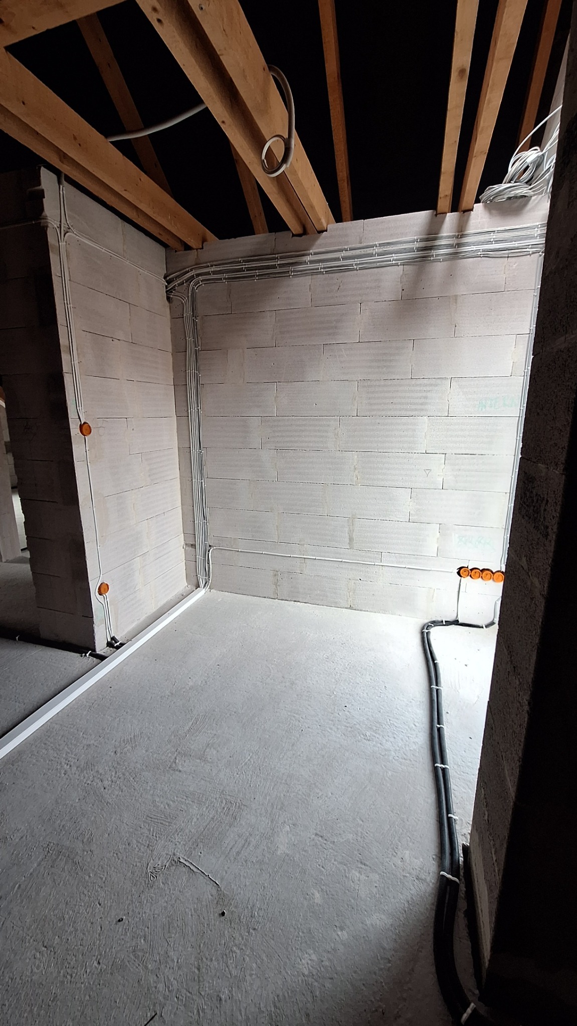 Surowy stan instalacji elektrycznej w nowym budynku: widoczne przewody w peszlach i rurkach na ścianach z betonu komórkowego i pod sufitem z drewnianych belek.