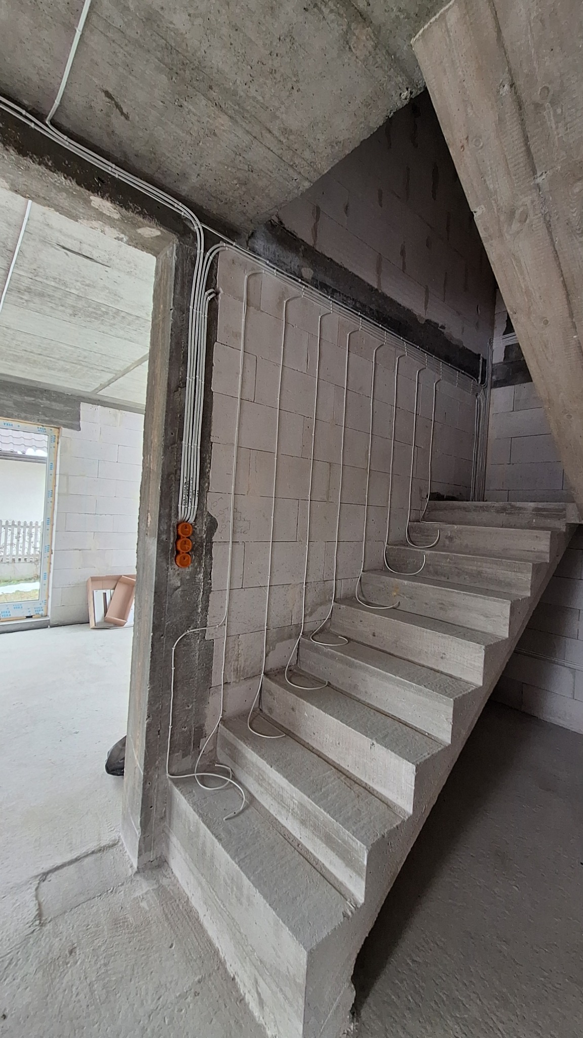 Surowe wnętrze w trakcie budowy: betonowe schody i ściany z betonu komórkowego z poprowadzonymi przewodami elektrycznymi w białych peszlach, widoczne puszki instalacyjne.