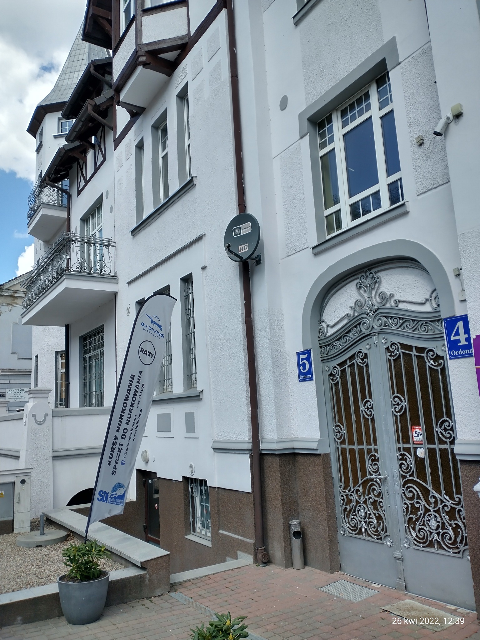 Flaga reklamowa z ofertą kursów nurkowania przed budynkiem z ozdobną bramą wejściową i numerami adresowymi 4 i 5.