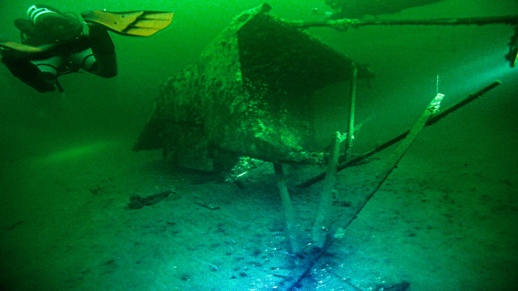 Nurek w żółtych płetwach eksploruje zatopioną konstrukcję pod wodą, oświetloną słabym światłem.