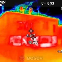 Termowizyjne zdjęcie budynku z zaznaczonymi punktami pomiaru temperatury ścian i fundamentów, ukazujące straty ciepła w kolorach od niebieskiego (najchłodniejsze) do czerwonego (najcieplejsze).