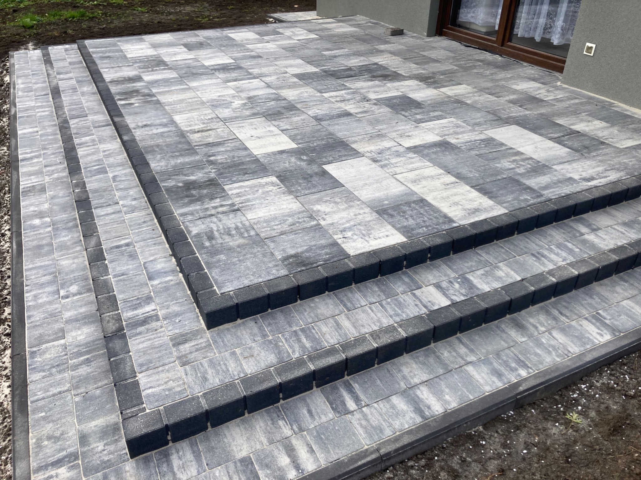 Schody i taras wyłożone szarą kostką o nieregularnym wzorze, obrzeża z ciemniejszej kostki, widok z góry.