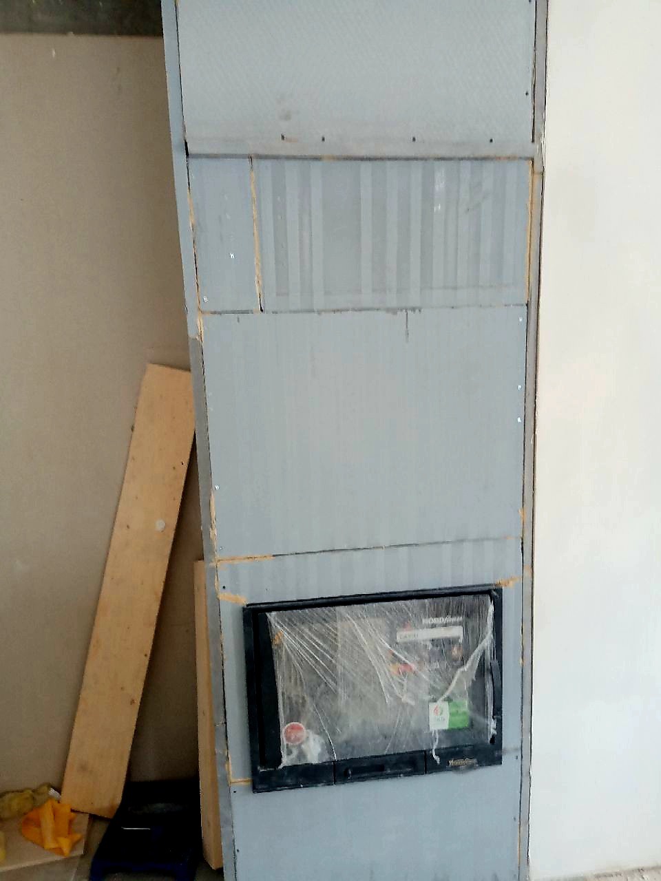 Montaż obudowy kominka z płyt kartonowo-gipsowych, widoczne łączenia i narożniki przed szpachlowaniem, obok oparta deska.