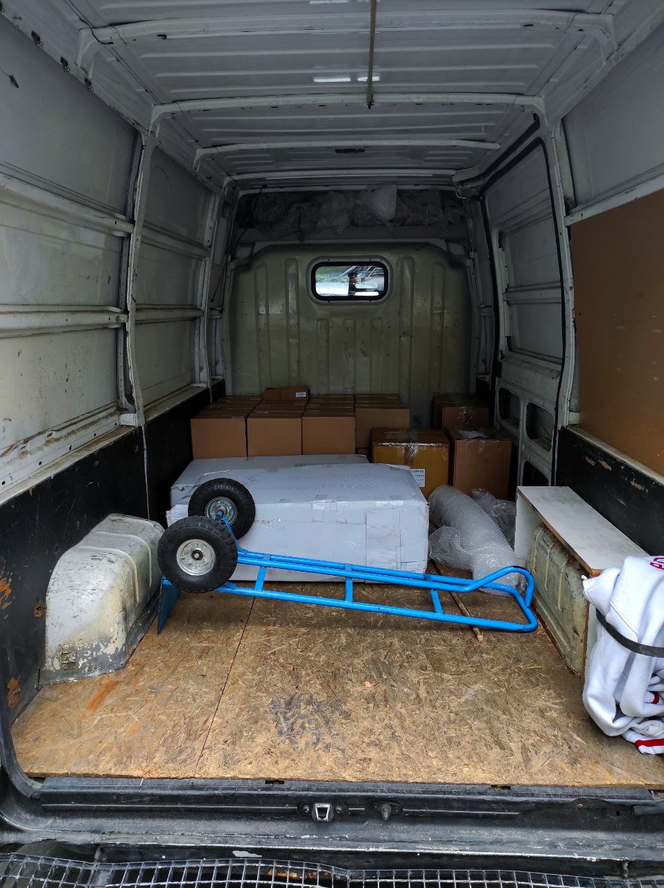 Wnętrze dostawczego busa z kartonami i wózkiem transportowym z niebieską ramą, przygotowanego do transportu.