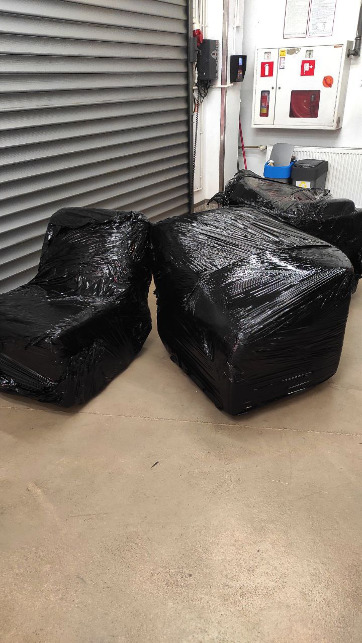 Meble zabezpieczone czarną folią stretch, przygotowane do transportu, widoczne elementy systemu przeciwpożarowego na ścianie.