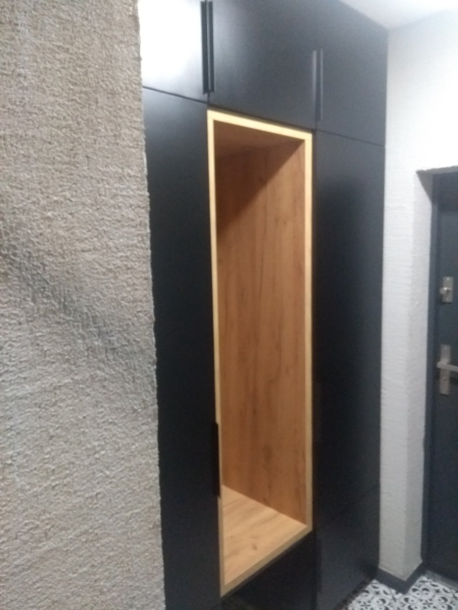Czarna szafa wnękowa z otwartą wnęką wykończoną drewnopodobnym materiałem, widoczna struktura ściany obok.