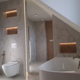 Elegancka łazienka na poddaszu z marmurowymi płytkami, podświetlanymi niszami i białą armaturą. Widoczny grzejnik drabinkowy, toaleta i wanna z złotą baterią.