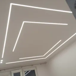 Nowoczesny sufit z liniowym oświetleniem LED w kształcie geometrycznym, widok z dołu, okno w tle, minimalistyczny design.